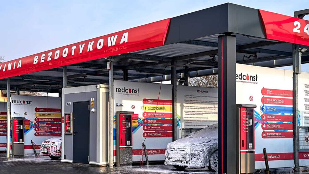 Myjnia bezdotykowa z nowoczesnymi urządzeniami do mycia samochodów. Widoczne informacyjne tablice oraz stacja z automatami, otoczenie czyste i zadbane. Idealne miejsce dla kierowców dbających o wygląd swojego pojazdu.