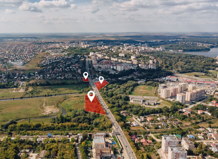 Widok z lotu ptaka na miasto z zaznaczonymi lokalizacjami, przedstawiający zabudowę miejską oraz tereny zielone. Mapa skupia się na obszarach, gdzie mogą znajdować się myjnie bezdotykowe, z charakterystycznymi markerami GPS.