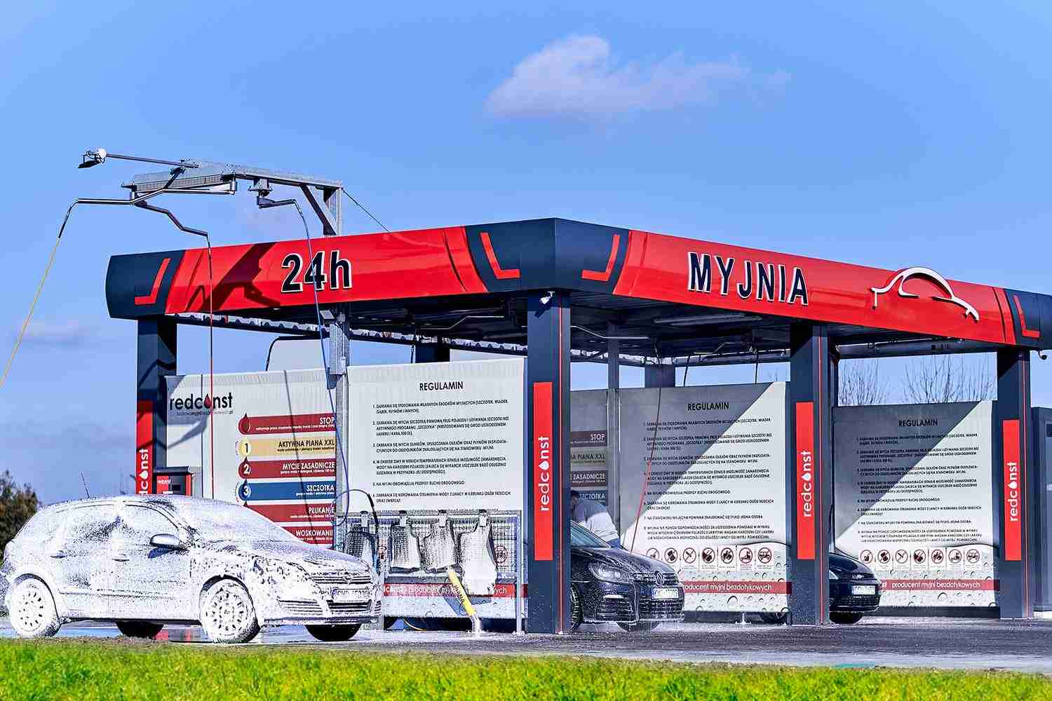 Bezdotykowa myjnia samochodowa działająca 24h, z widocznymi samochodami pokrytymi pianą. W tle zasady korzystania z myjni. Idealna dla tych, którzy szukają efektywnego rozwiązania do mycia auta.