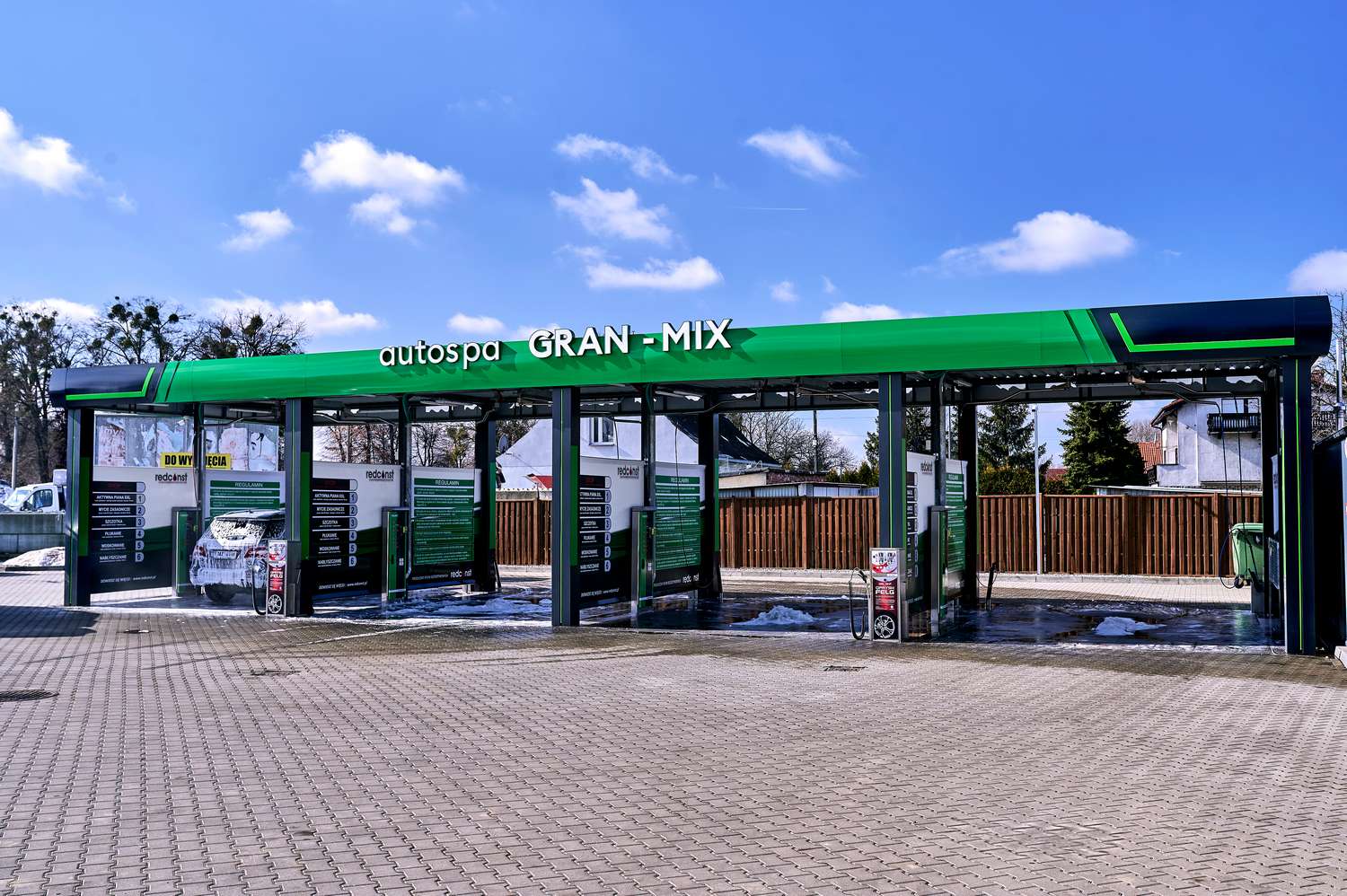 Nowoczesna myjnia bezdotykowa "GRAN-MIX" z różnymi stanowiskami do mycia samochodów, z osłoniętą powierzchnią i ekologicznymi rozwiązaniami. Przestrzeń otoczona pogodnym niebem i zielonym otoczeniem, stwarzająca komfortowe warunki dla użytkowników myjni.
