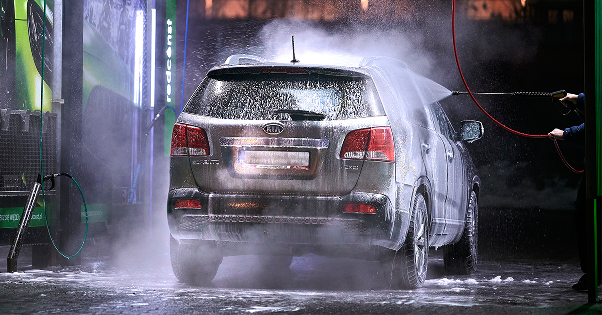 Samochód SUV podczas mycia w myjni bezdotykowej. Woda i piana wykonują czyszczenie karoserii, a w tle widoczne są sprzęty i oświetlenie myjni. To idealny przykład efektywnej pracy producenta myjni bezdotykowej.